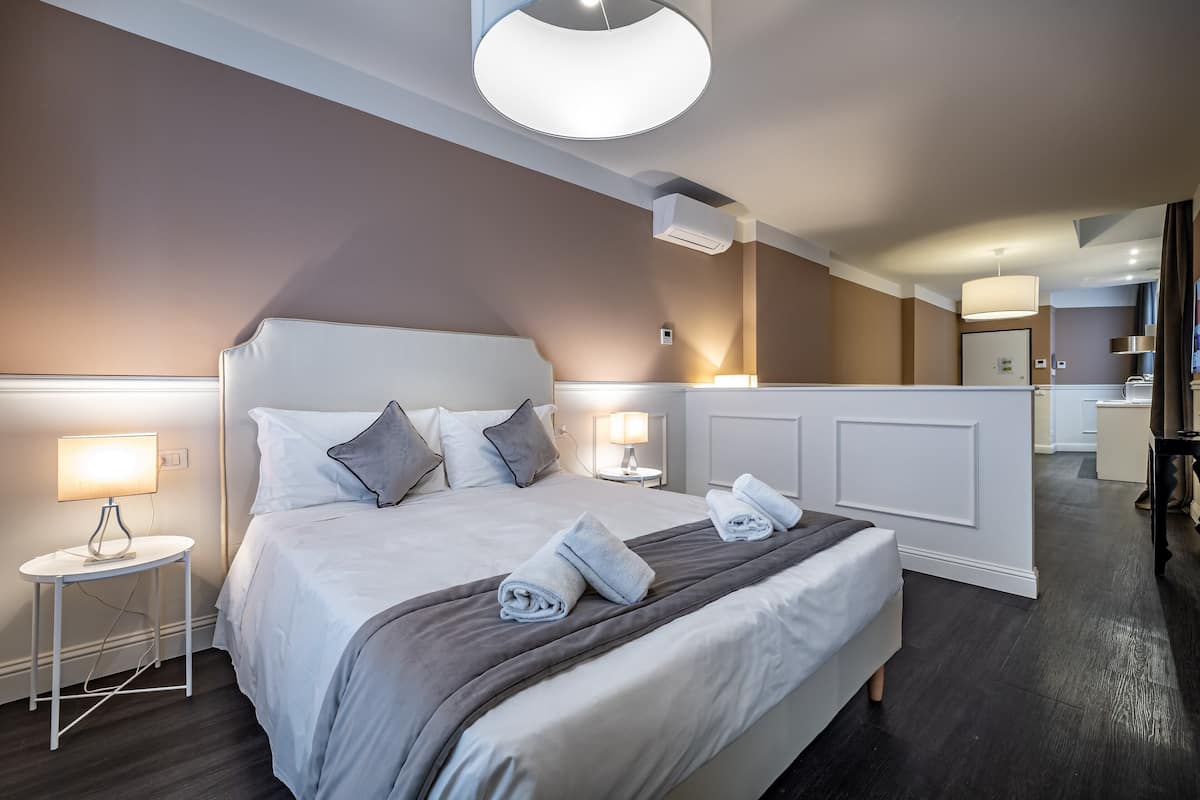 Une chambre d’hôtel moderne avec un grand lit, des lampes de chevet, un luminaire rond au plafond et une vue sur la salle de bain attenante.