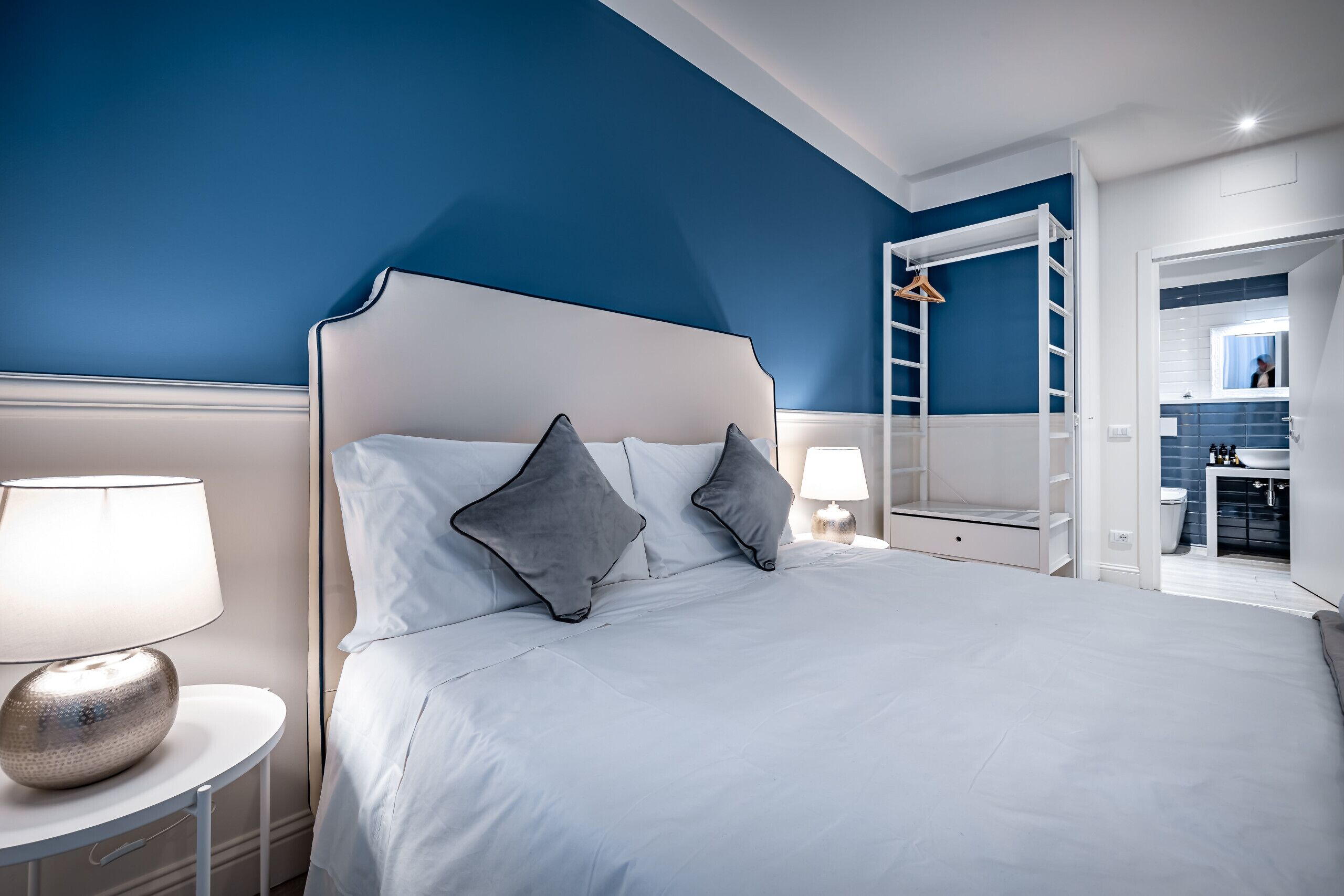 Een slaapkamer met een bed, nachtkastjes, een kledingkast, en een badkamer zichtbaar door een geopende deur.