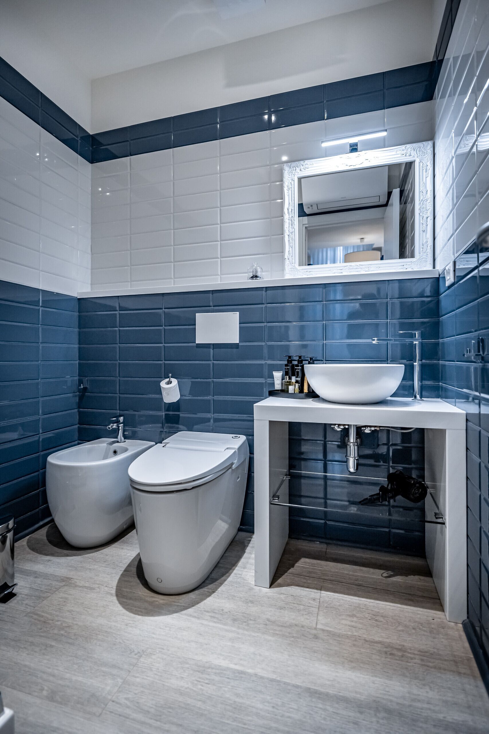 Ein modernes Badezimmer mit einem weißen Waschbecken, zwei Toiletten und einem Spiegel über dem Waschbecken.