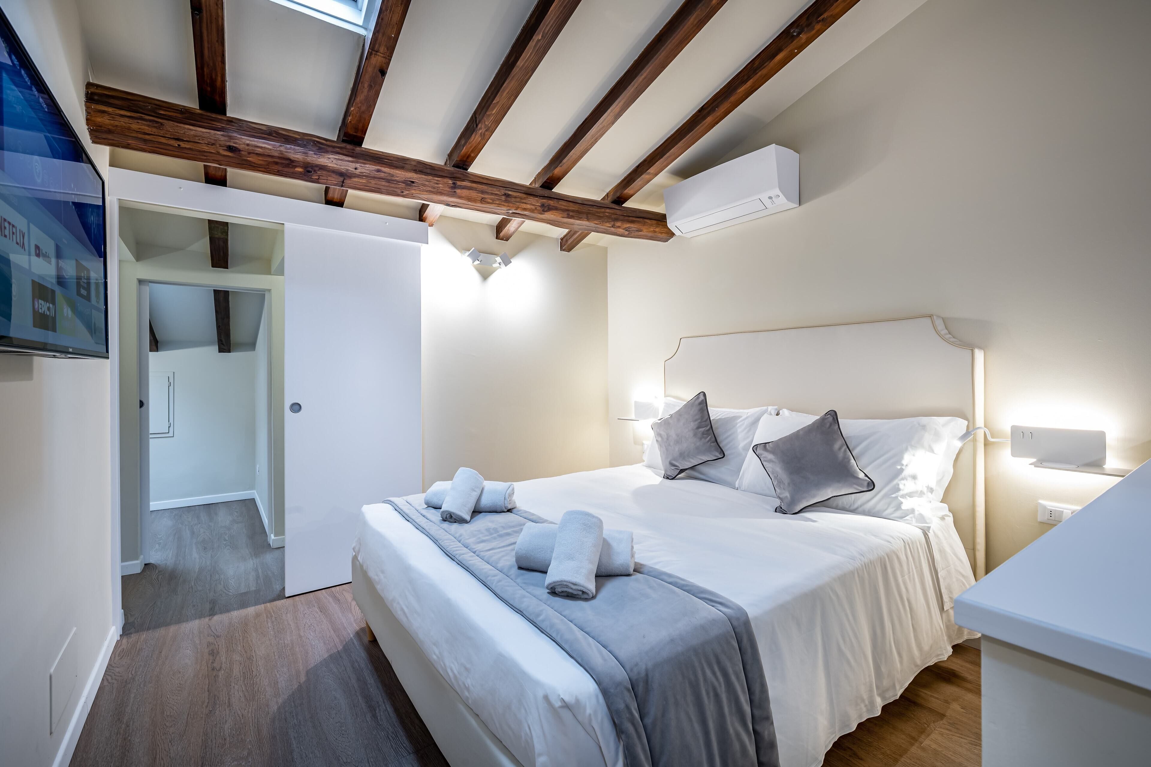 Ein Schlafzimmer mit Holzboden, einem Bett mit Kissen und Handtüchern, einem Nachttisch und einer Wand-Klimaanlage.