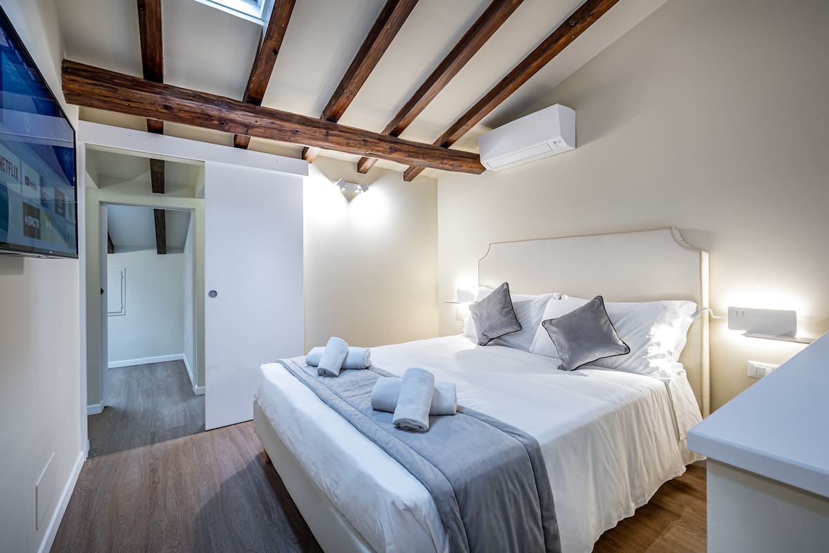 Une chambre avec un plafond en bois, un lit avec des oreillers et des serviettes, une table de chevet et un climatiseur fixé au mur.