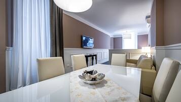 A dining area with a white table, beige chairs, a decorative bowl, and a television on the wall.