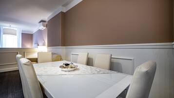 A dining area with a white table, beige chairs, and a bowl of fruit.