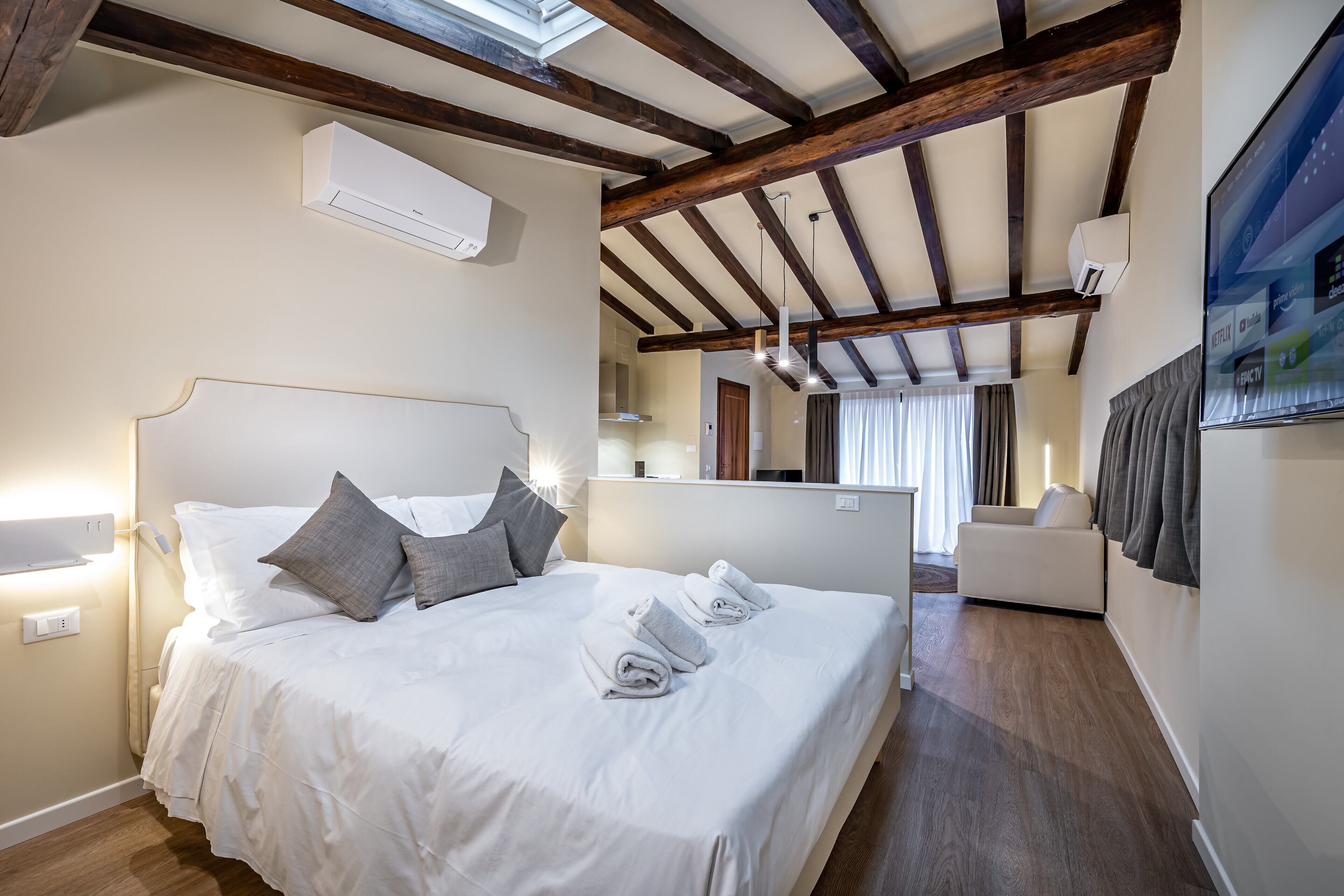 A hotel room with a large bed, a flat-screen TV, a wooden ceiling, and a modern design.