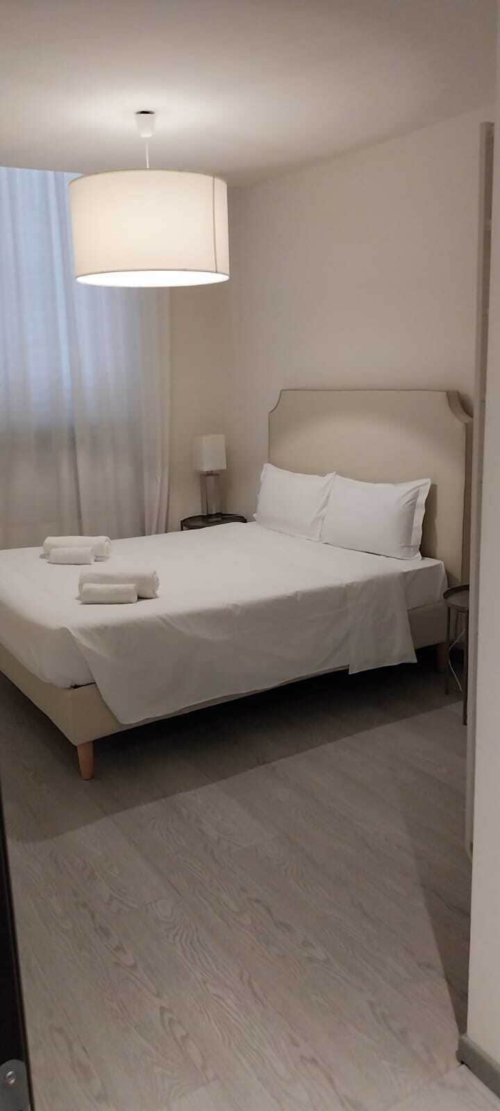Un lit bien fait, avec du linge de lit blanc et des oreillers, une lampe de chevet et une fenêtre avec des rideaux.
