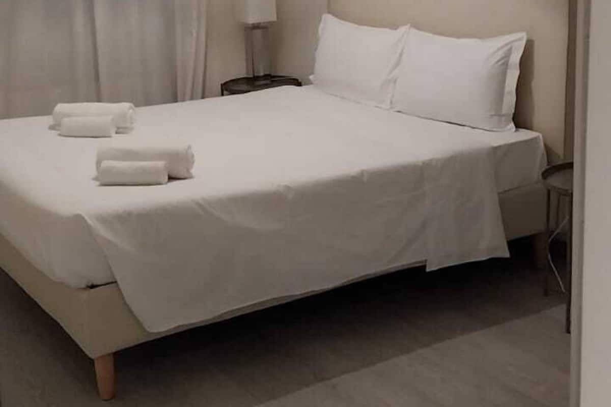 Un lit bien fait, avec du linge de lit blanc et des oreillers, une lampe de chevet et une fenêtre avec des rideaux.