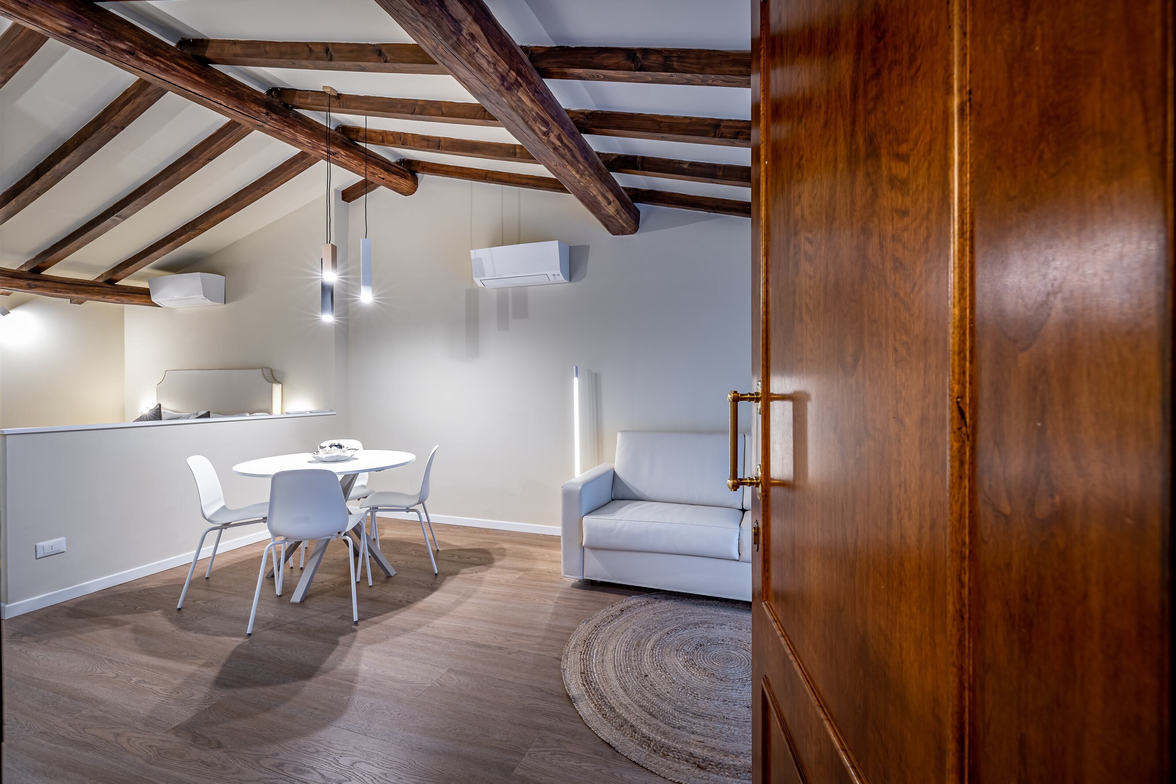 A modern kitchen with white cabinetry, a dining area with a round table and chairs, and a wooden ceiling with exposed beams.