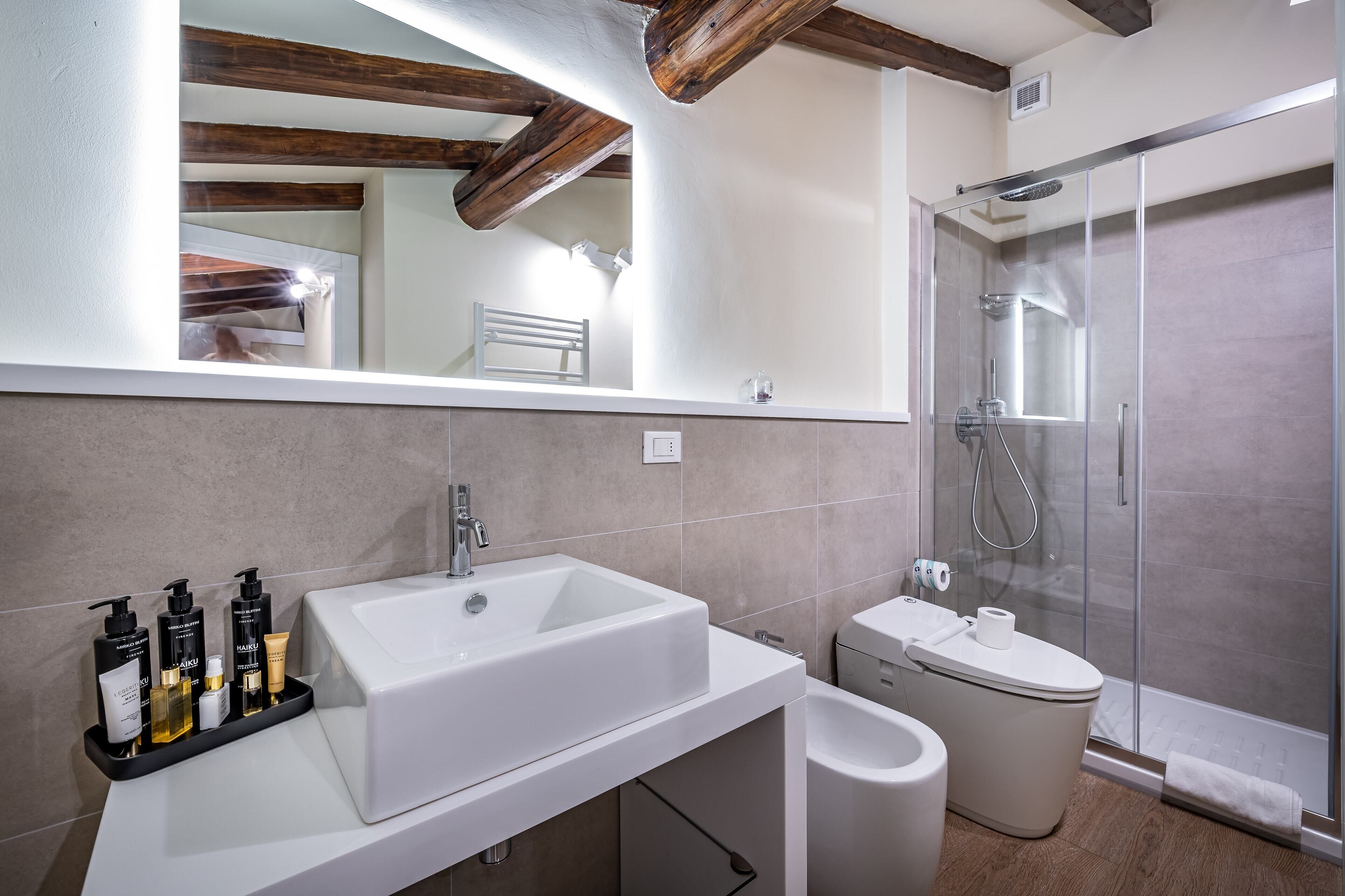 A modern bathroom with a large white sink, a glass-enclosed shower, and a toilet.