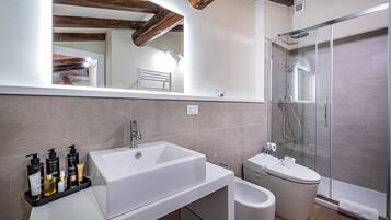A modern bathroom with a large white sink, a glass-enclosed shower, and a toilet.