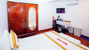 A hotel room with a wooden wardrobe, a bed with a white and gold bedspread, a small table with toiletries, a mounted TV, and a trash bin. - The Rice Hotel & Tour - 191 Bui Vien (Ho Chi Minh City)