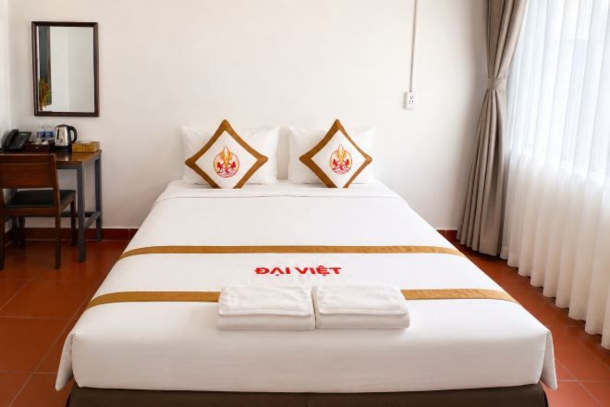 Quarto de hotel com cama, escrivaninha e cadeira.