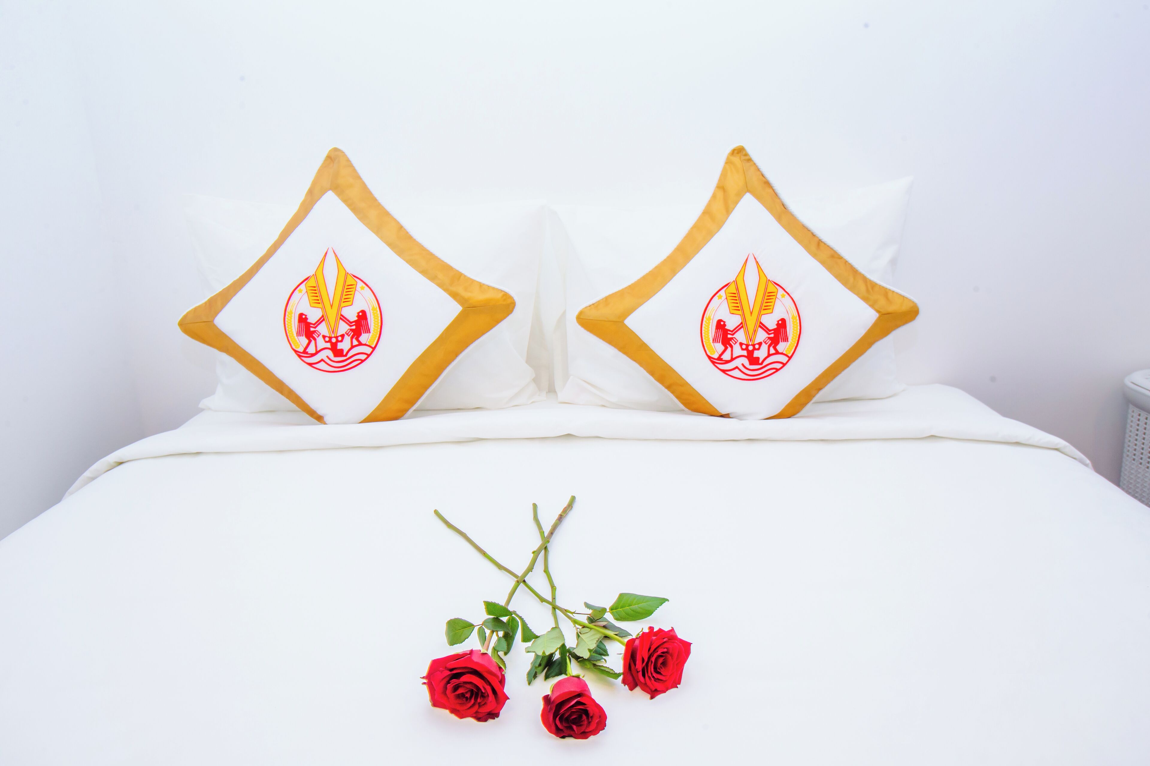 A bed with white bedding and two pillows featuring a red and yellow emblem.