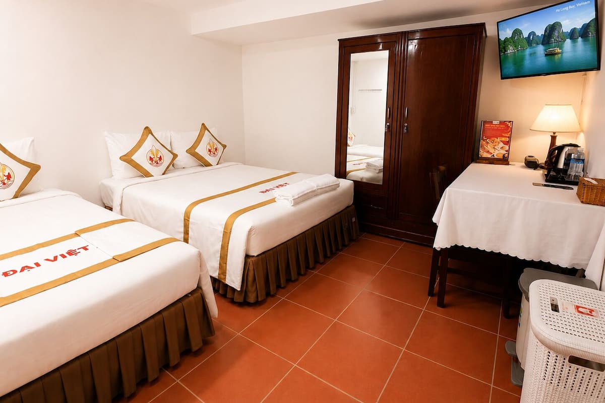 A hotel room with two beds, a TV, a desk with a lamp, and a view of a coastal landscape.