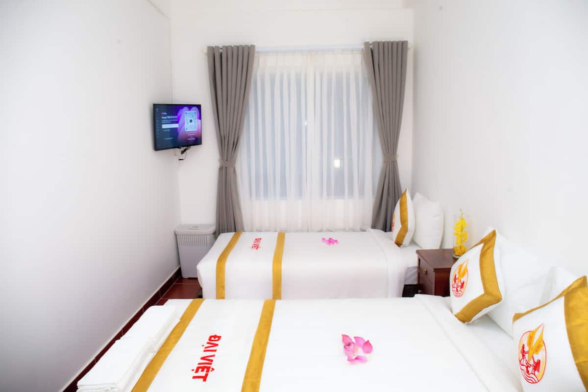 A hotel room with two beds, a TV on the wall, and a window with curtains.