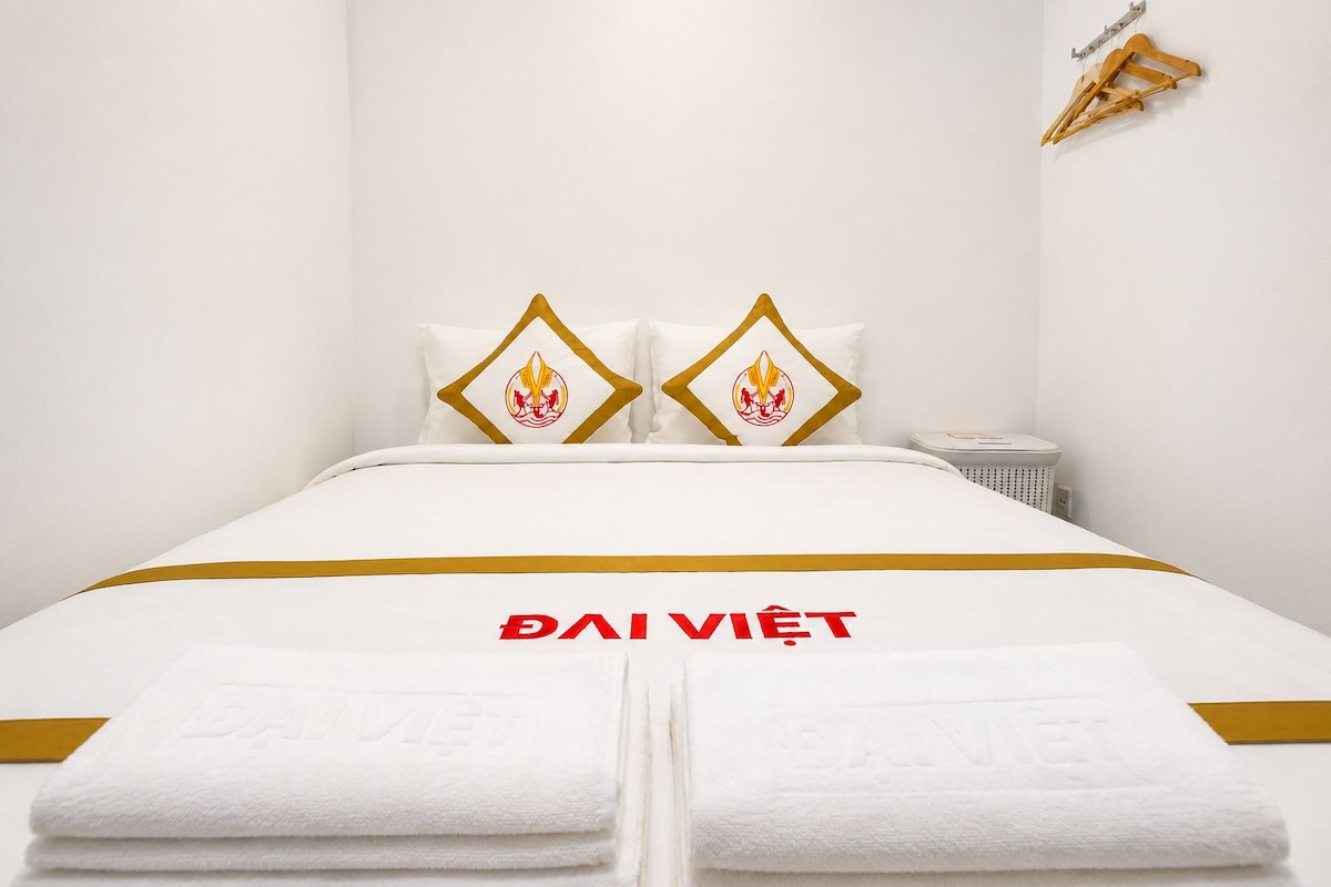 Una habitación de hotel con cama, almohadas con un logotipo, una mesita de noche y un perchero para toallas en la pared.