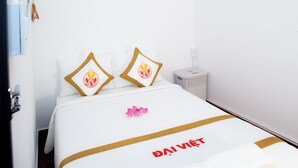 A hotel room with a bed featuring a white bedspread with gold trim and a logo, two pillows with a flame design, and a pink flower on the bed. - The Rice Hotel & Tour - 191 Bui Vien (Ho Chi Minh City)