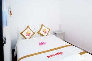 A hotel room with a bed featuring a white bedspread with gold trim and a logo, two pillows with a flame design, and a pink flower on the bed. - The Rice Hotel & Tour - 191 Bui Vien (Ho Chi Minh City)