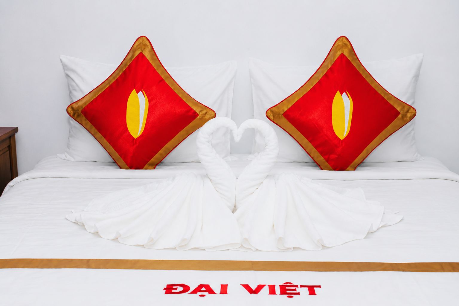 A bed with white bedding and two red pillows with gold trim.
