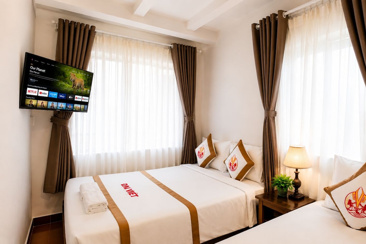 Una habitación de hotel con dos camas, un televisor montado en la pared y cortinas en las ventanas.