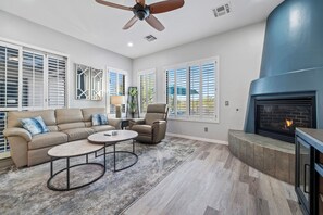 A spacious living room with a beige sectional sofa, a round coffee table, a recliner, and a fireplace.
