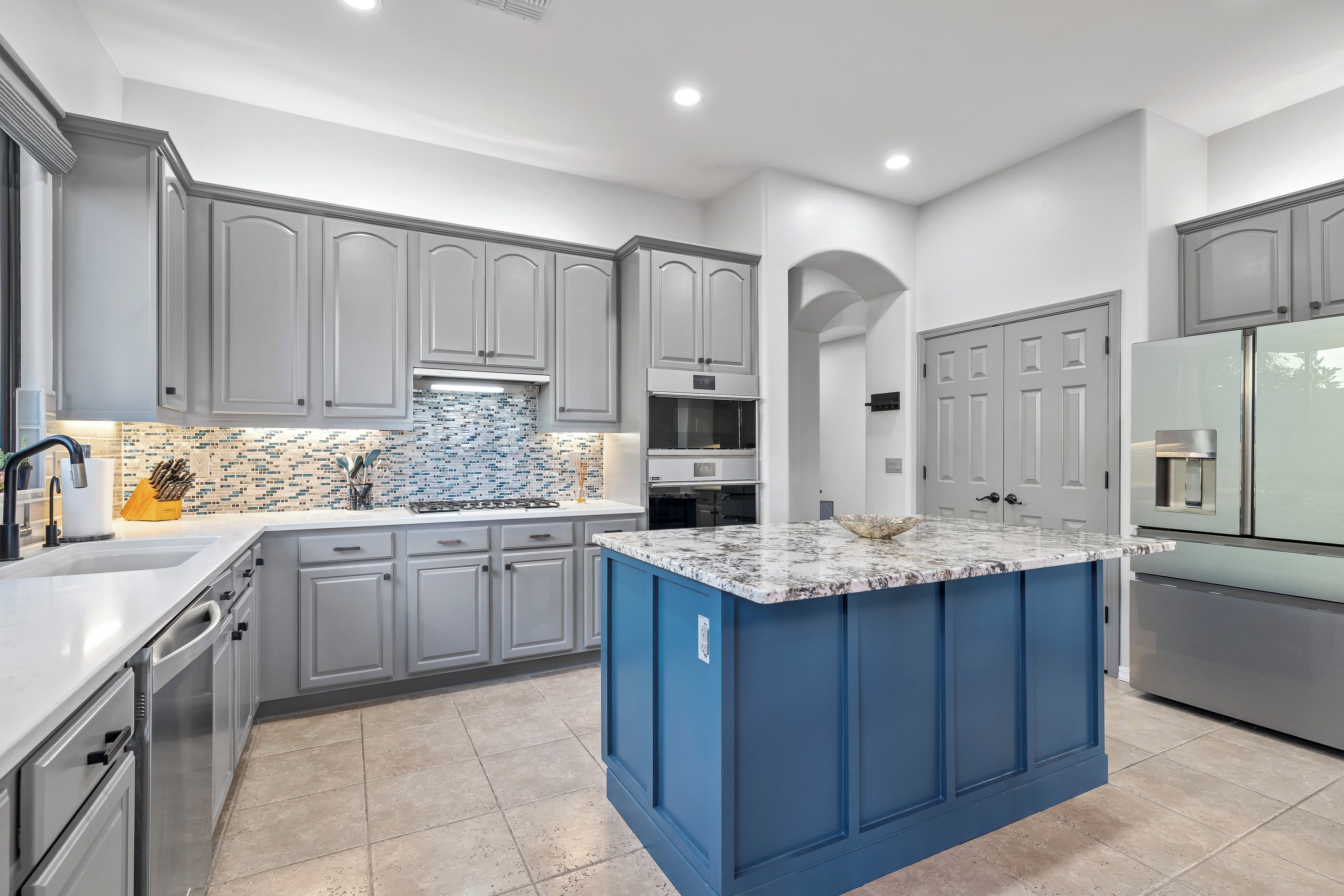 A modern kitchen with grey cabinetry, a blue island, and a tiled backsplash.