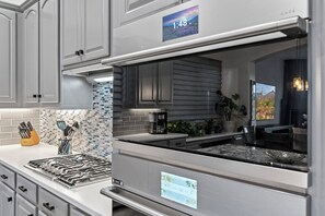 Una cucina moderna con elettrodomestici in acciaio inox, una sveglia digitale e un pannello di piastrelle blu e bianche.