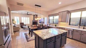 Una cocina moderna con armarios oscuros, una isla grande y una zona de comedor con sofá y sillas.
