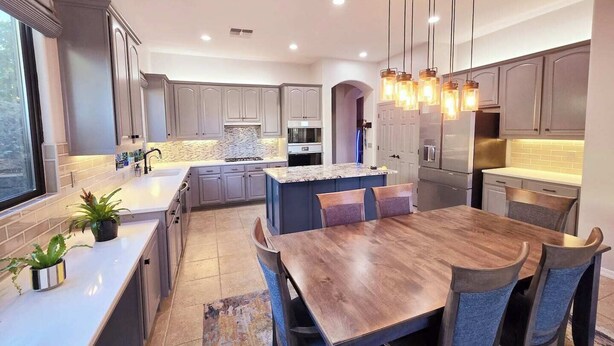 Una cocina moderna con gabinetes grises, una isla central e iluminación colgante.