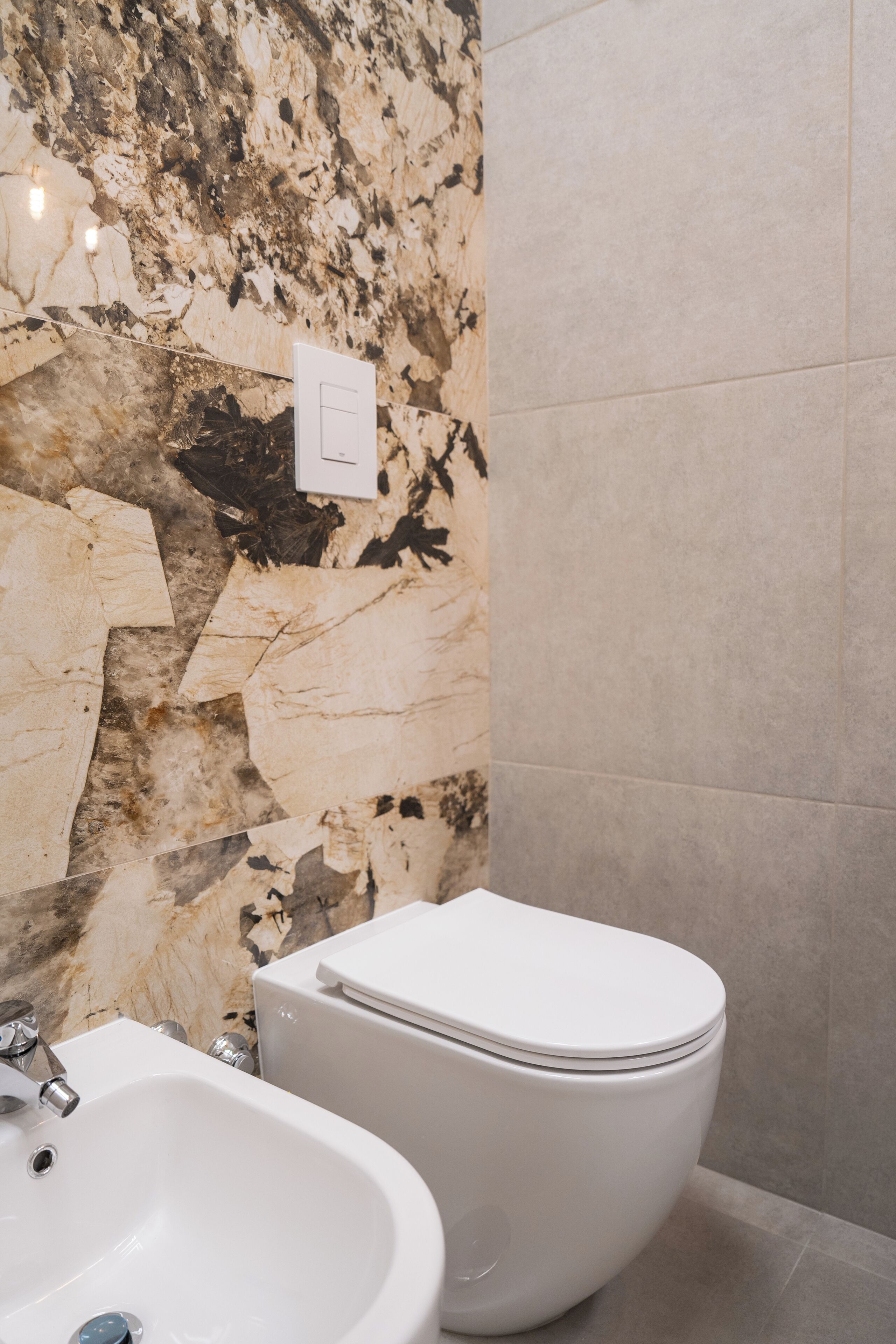 Une salle de bain avec un mur en marbre, un lavabo blanc et des toilettes.