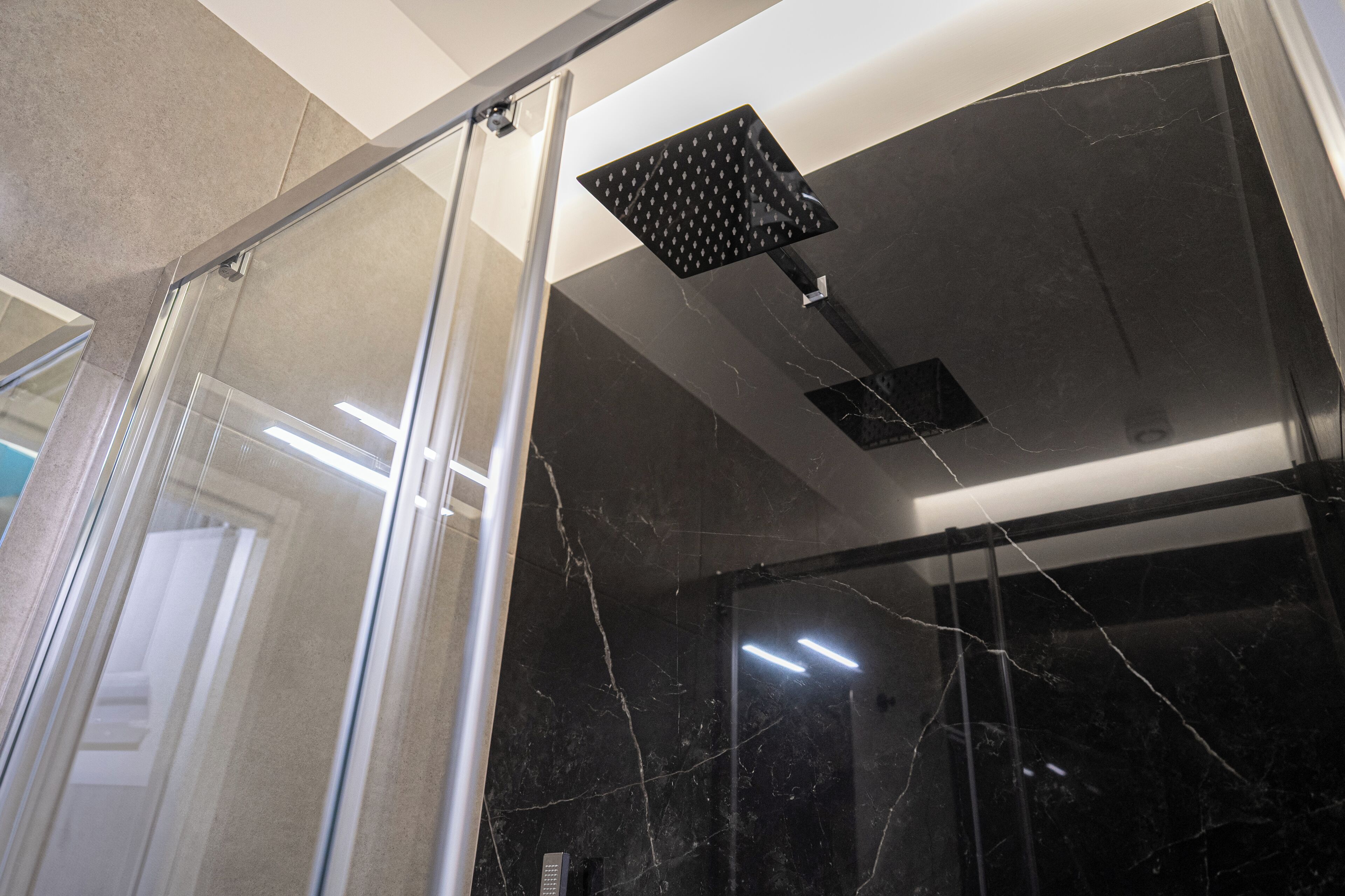 Ein modernes Badezimmer mit einer gläsernen Duschkabine, schwarzen Marmorwänden und einem sichtbaren Bedienfeld.