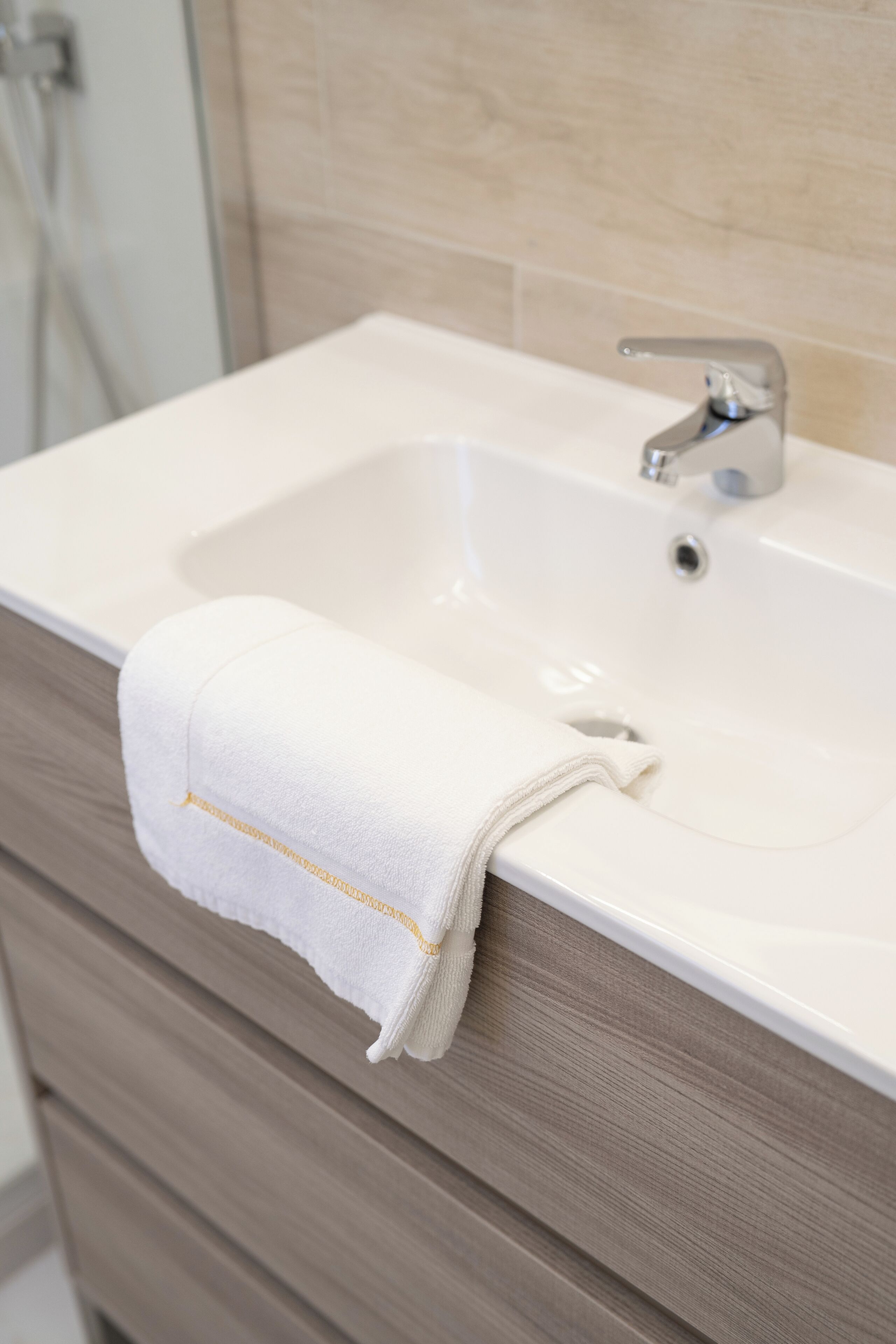 Een badkamer met een witte wasbak, een handdoek en een houten kastje.