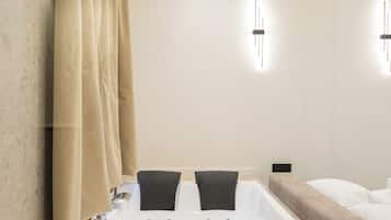 Ein modernes Badezimmer mit freistehender Badewanne, Holzboden, beige Vorhängen und schlichten Wandleuchten.