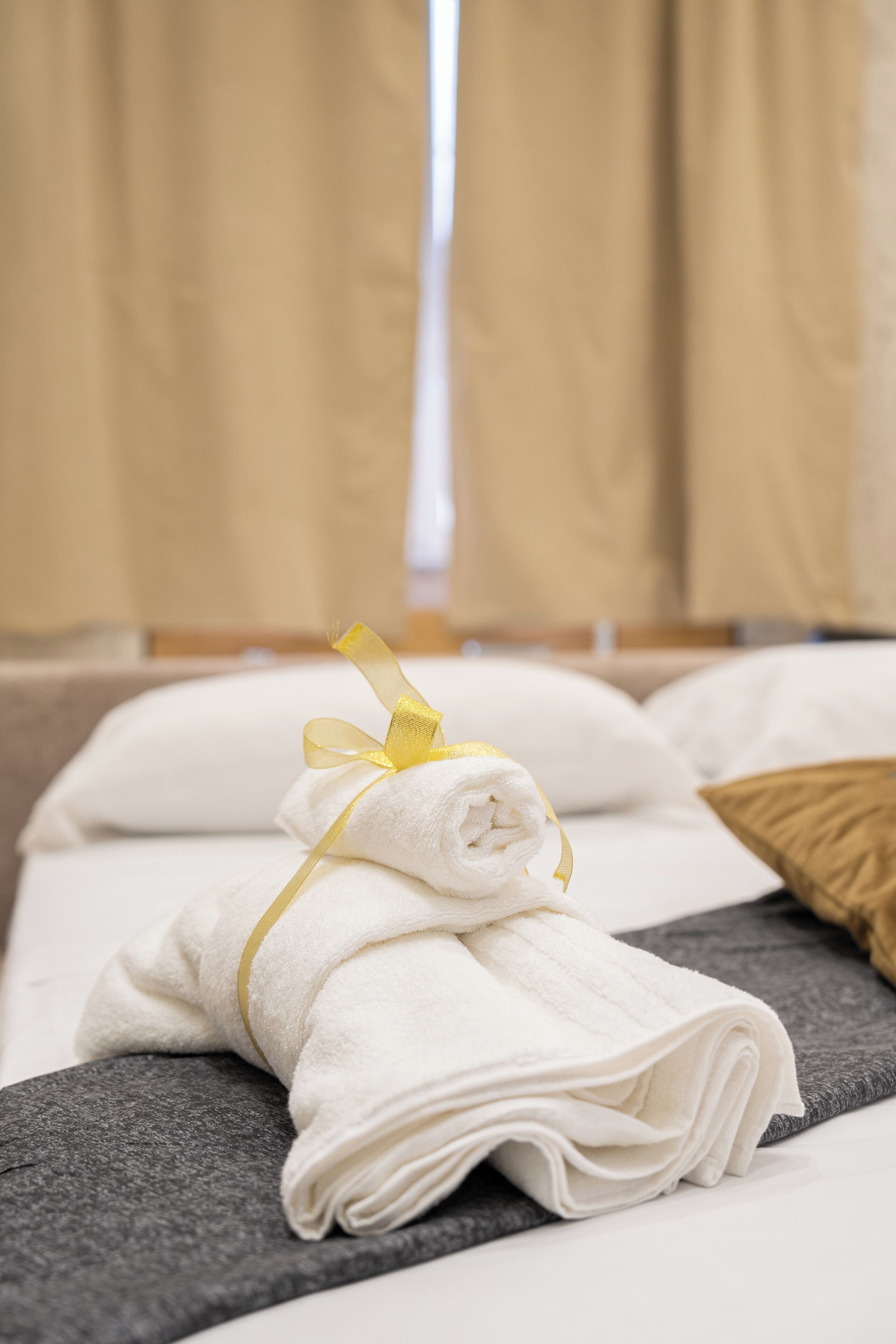 Un letto rifatto con asciugamani bianchi e un nastro giallo, una coperta grigia e un cuscino marrone.