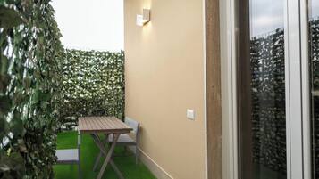 A small outdoor patio with a wooden table and chairs, surrounded by a green hedge.