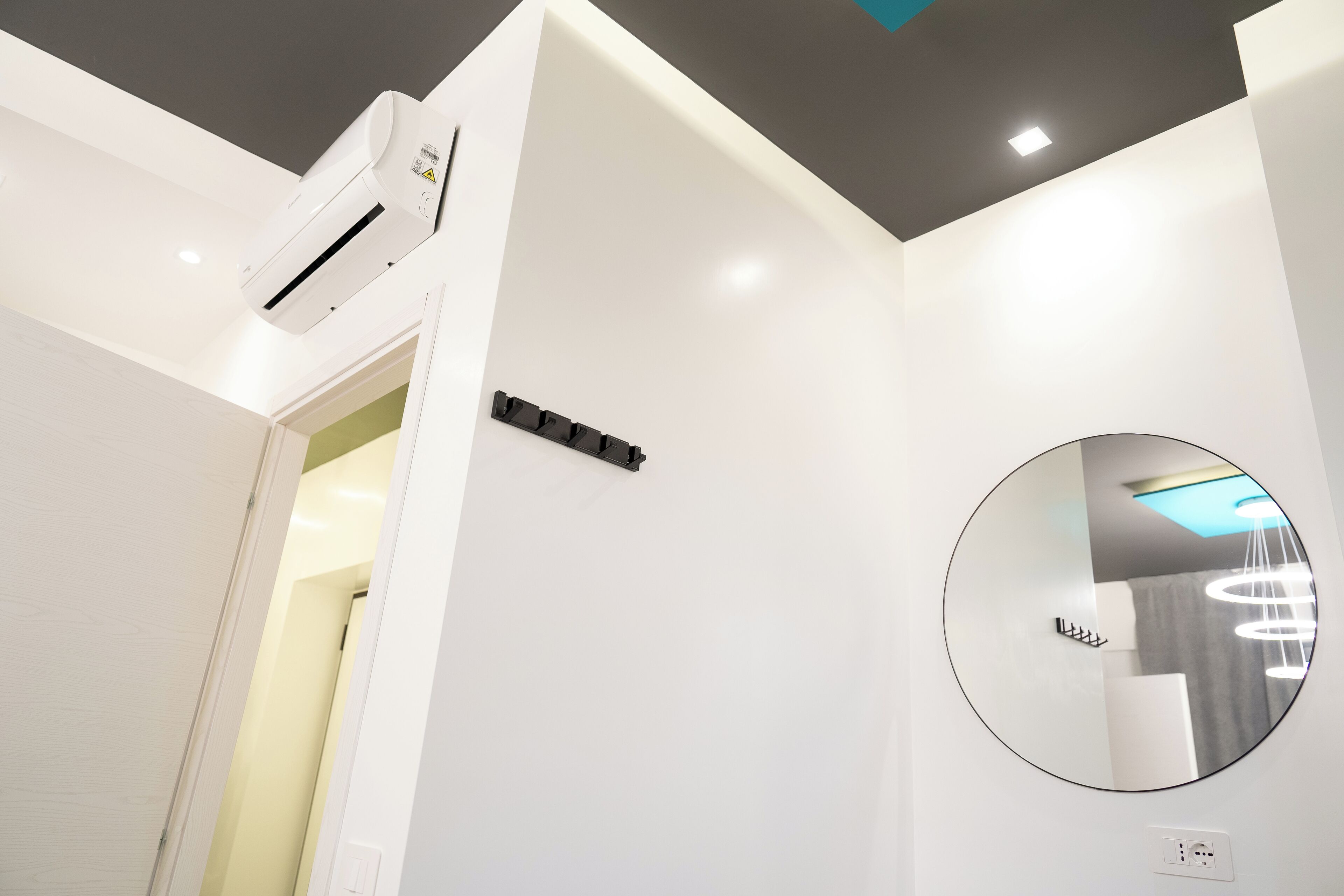 A modern bathroom with a white ceiling, a round mirror, and a ceiling-mounted air conditioner.