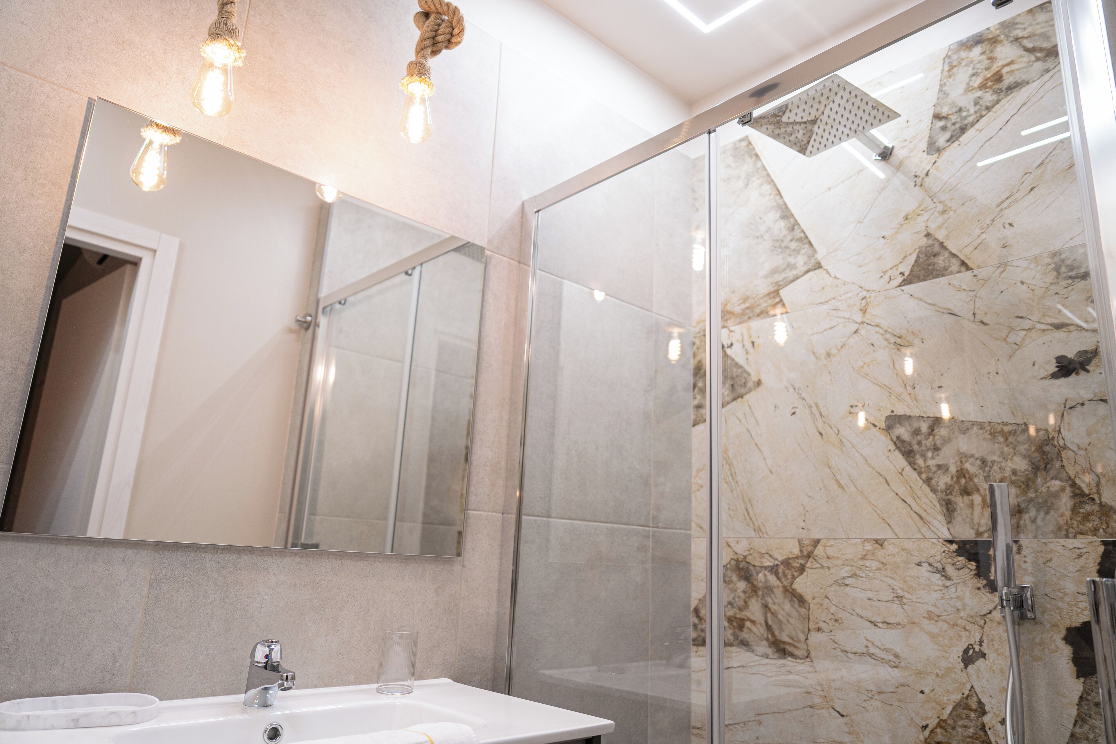 Un baño moderno con cabina de ducha de vidrio, un espejo grande y un lavamanos blanco.
