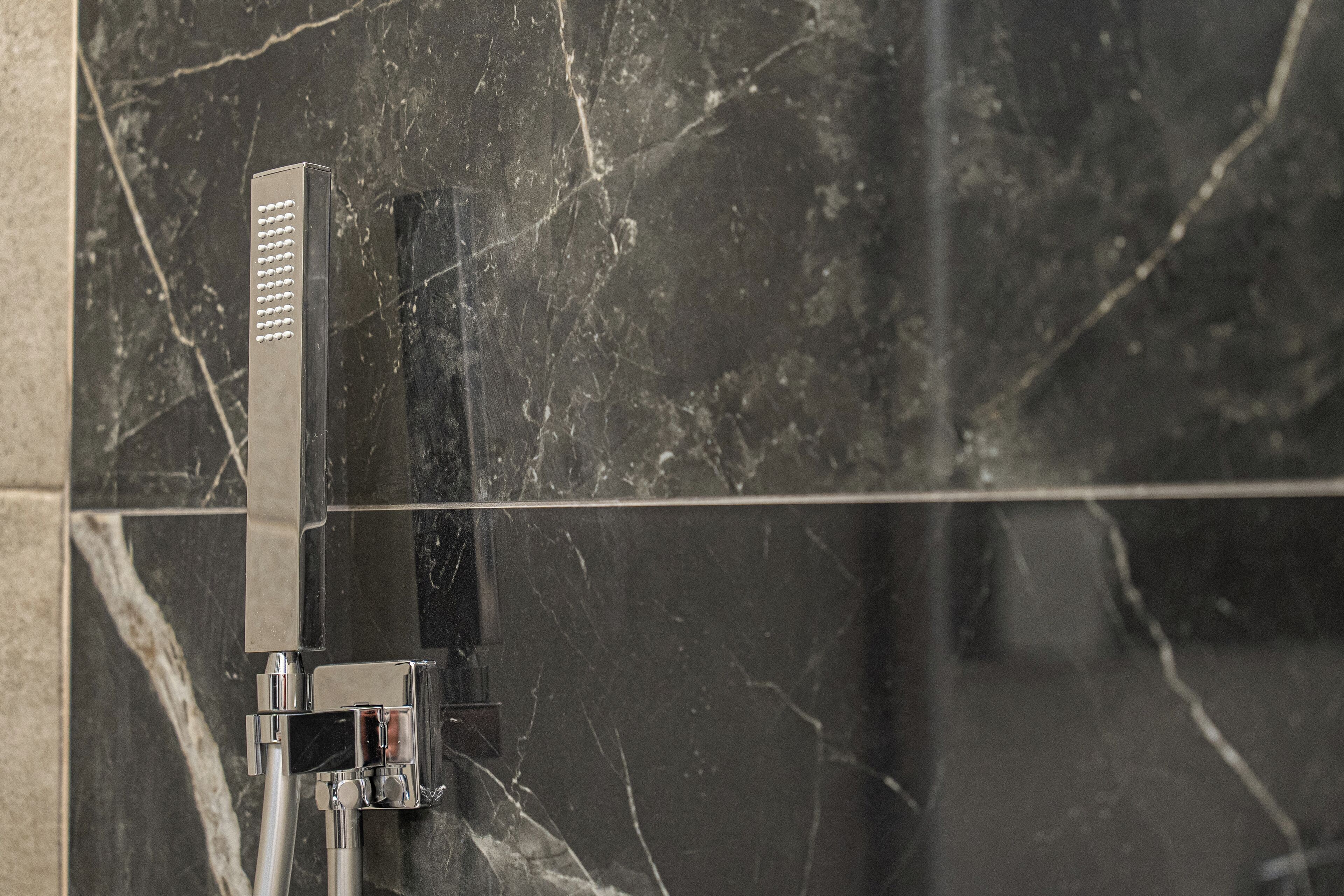 A modern showerhead mounted on a wall with a marble-like texture.