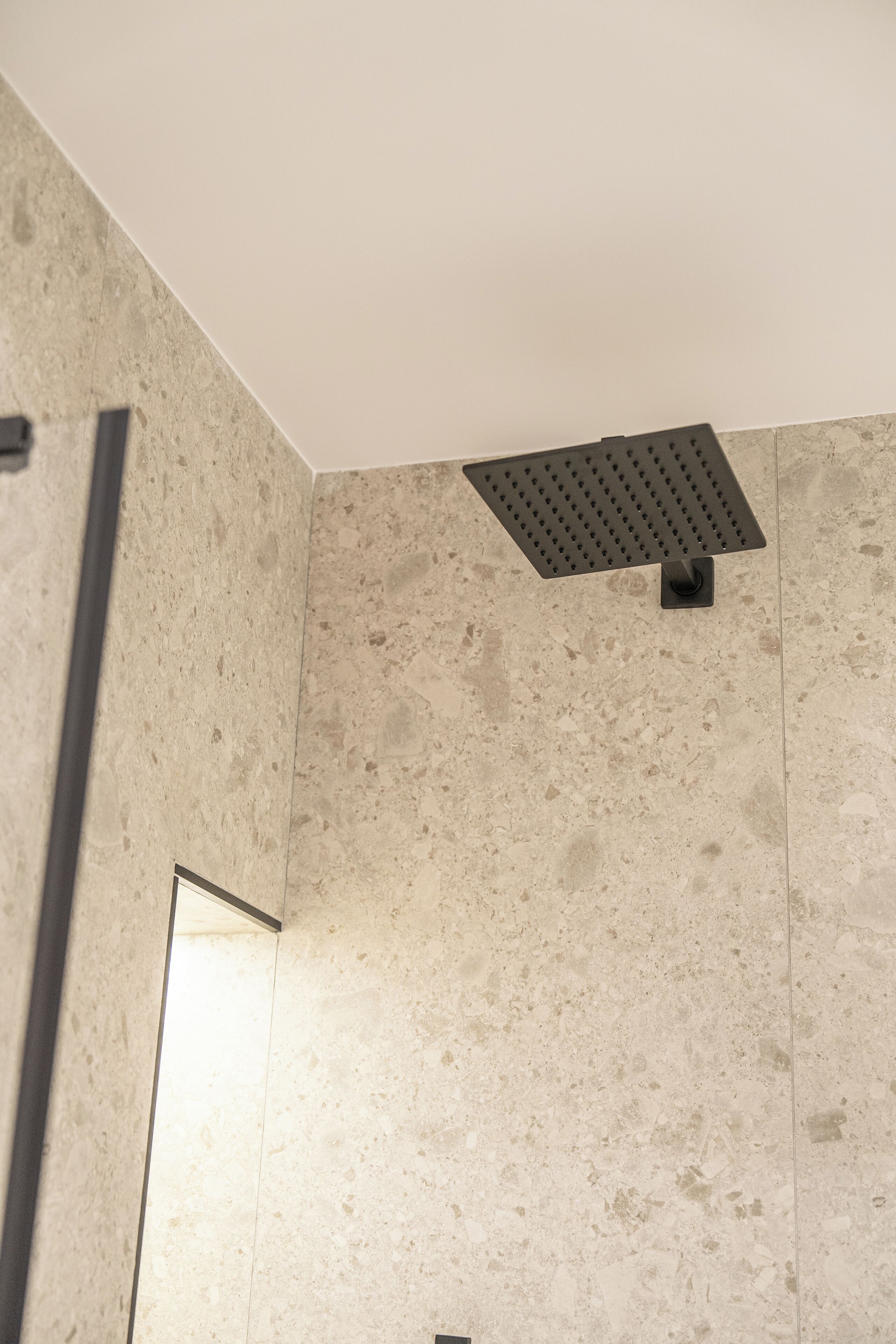 A shower area with a rectangular showerhead mounted on a textured wall.