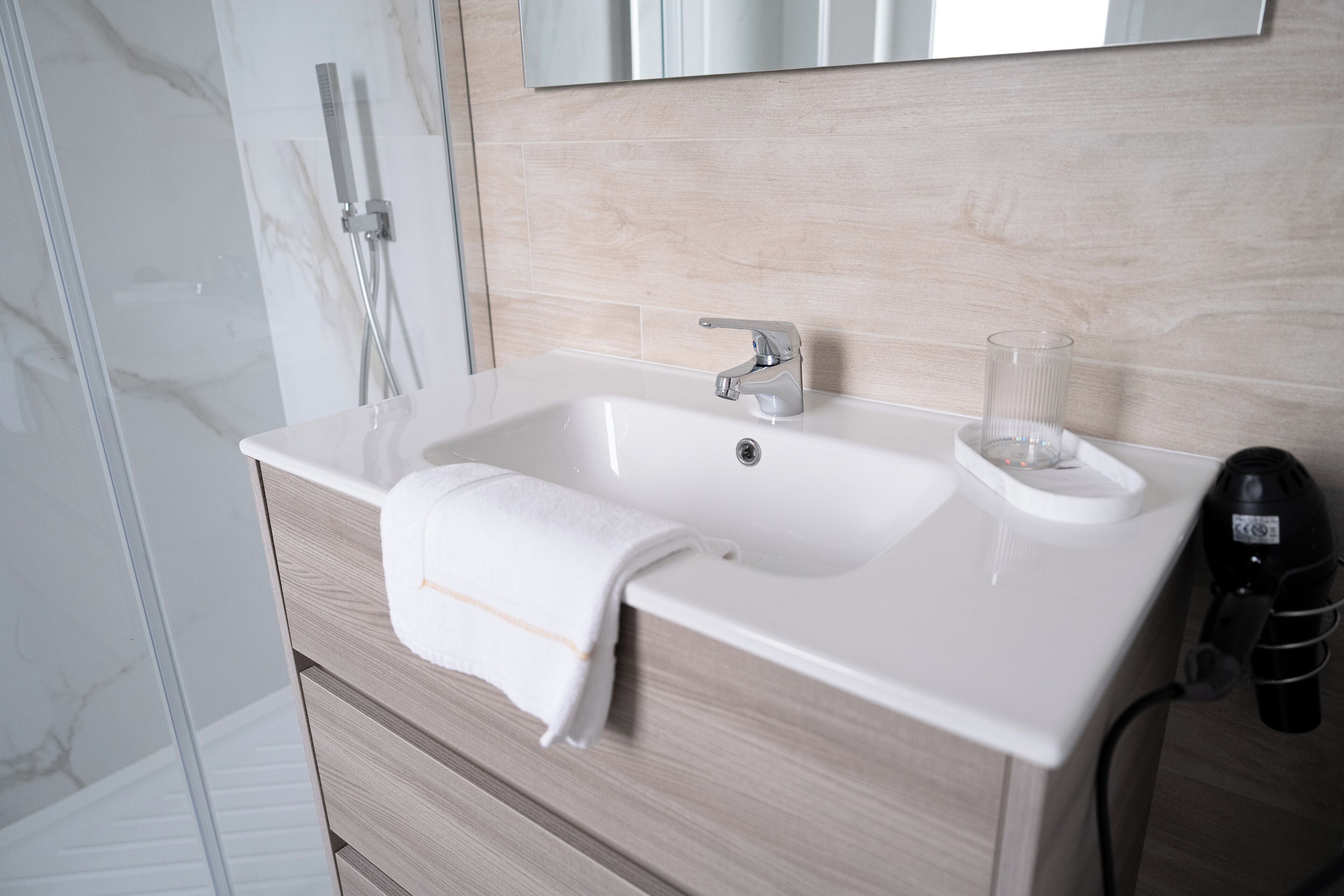 A bathroom with a white sink, a towel, and a glass of water on the counter.