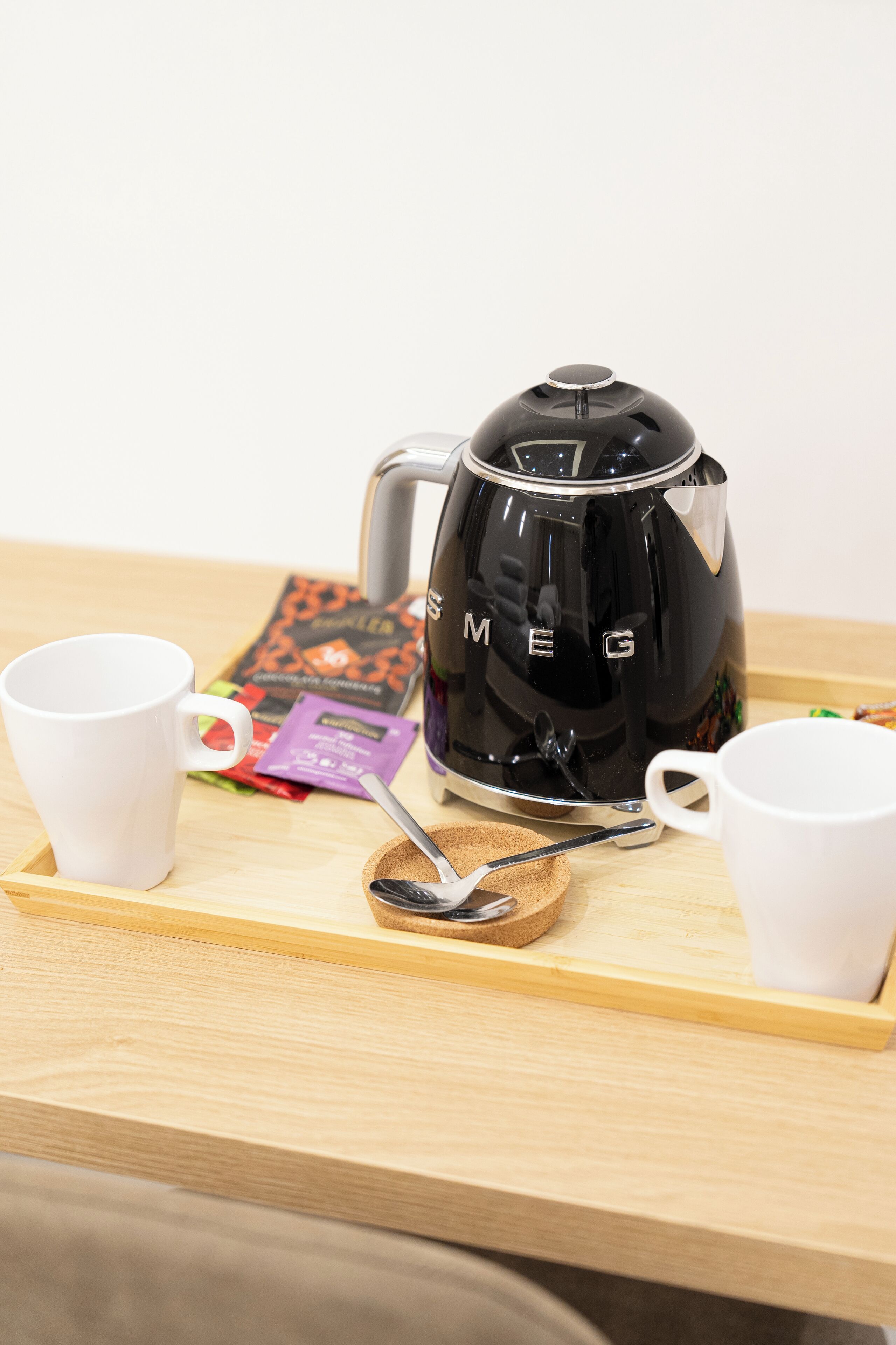A coffee maker on a tray with two white cups and a spoon.