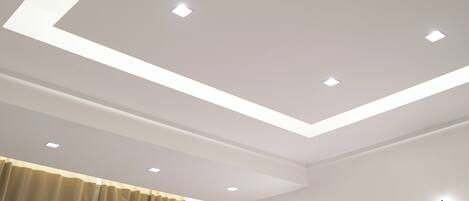 Une chambre moderne avec un plafond en retrait, une fenêtre avec des rideaux et des luminaires fixés au mur.