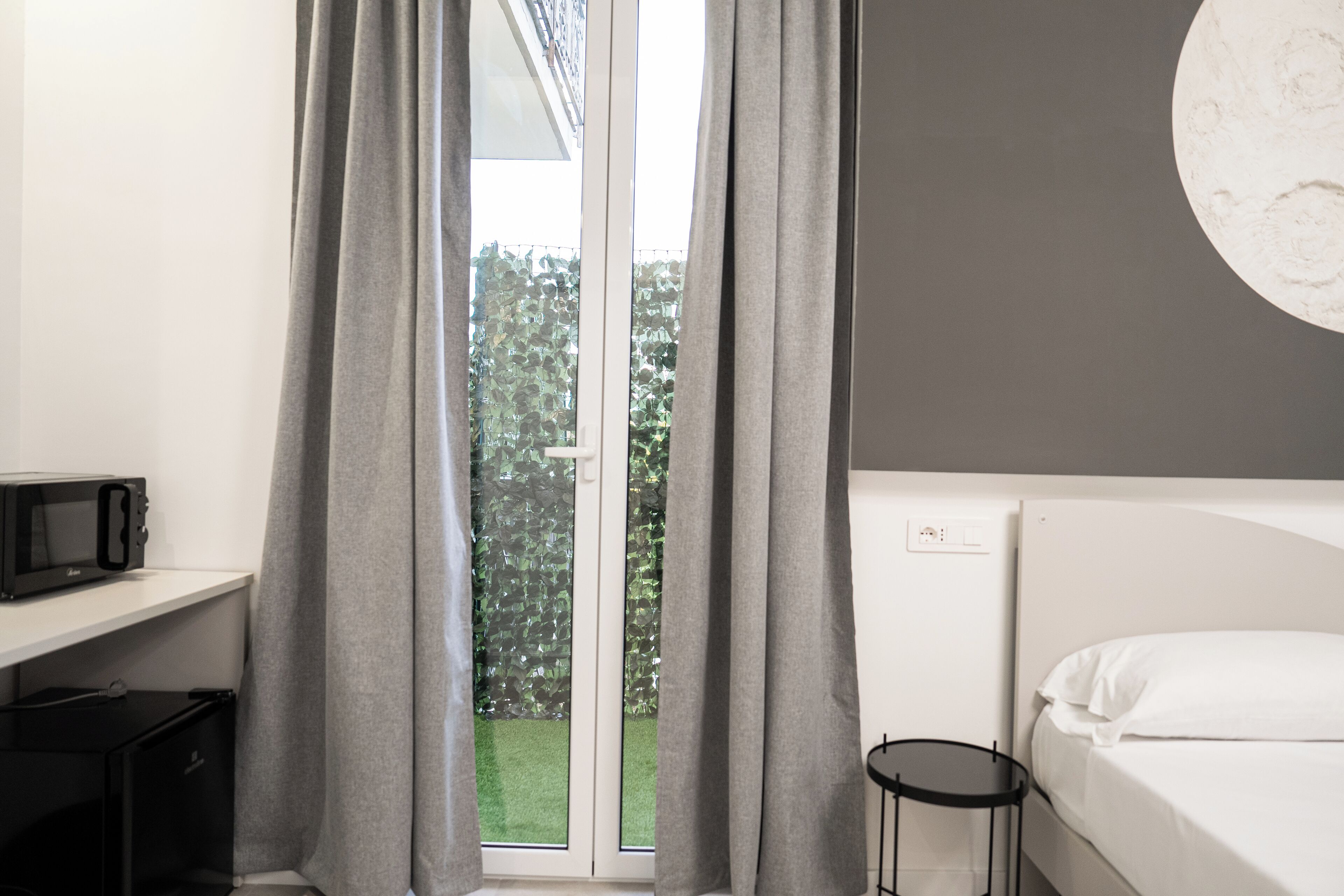 A hotel room with a bed, a small table, a microwave, and a window with curtains.