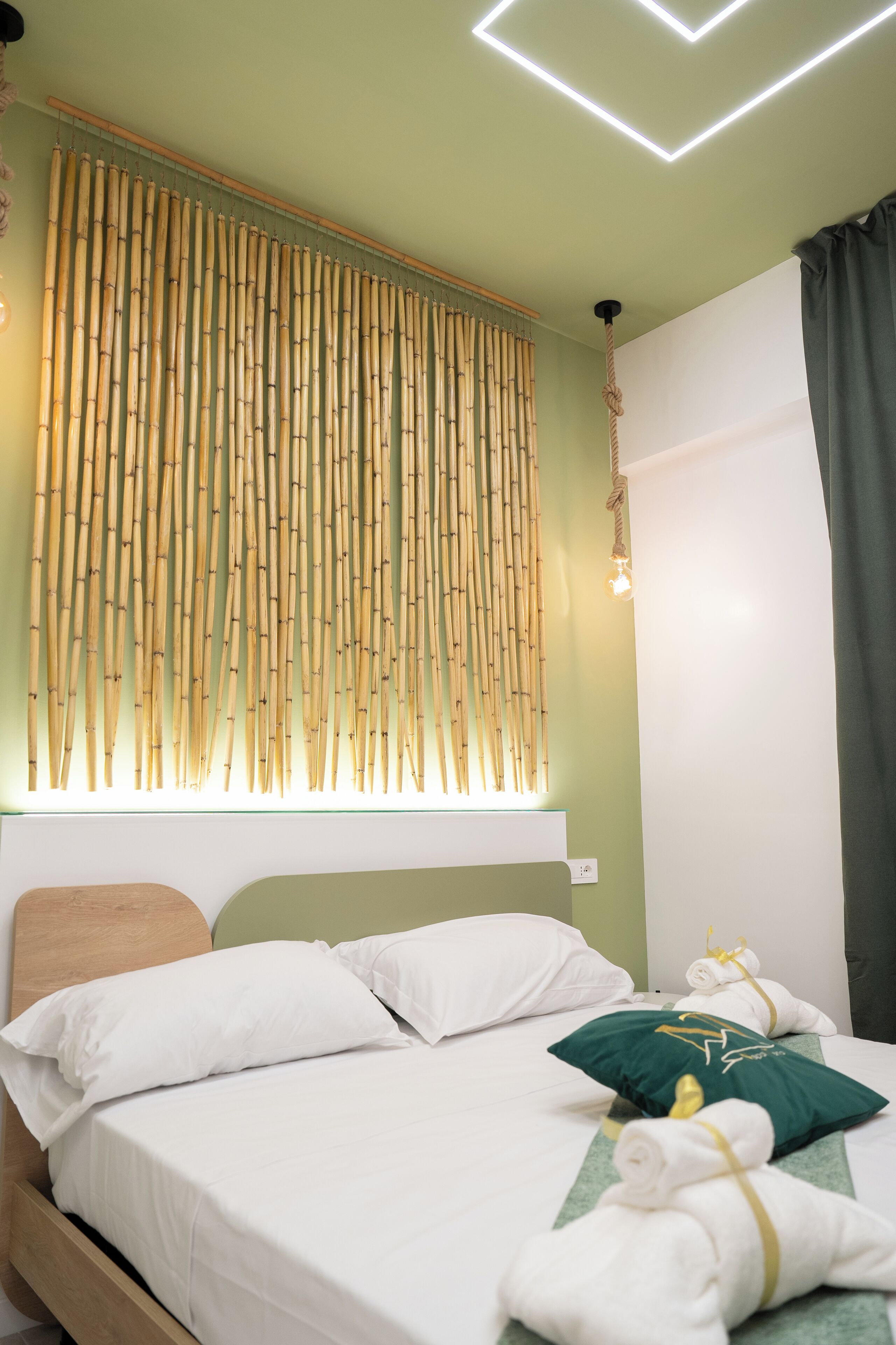 A neatly made bed with white linens, a green pillow, and a rolled towel on a wooden headboard.