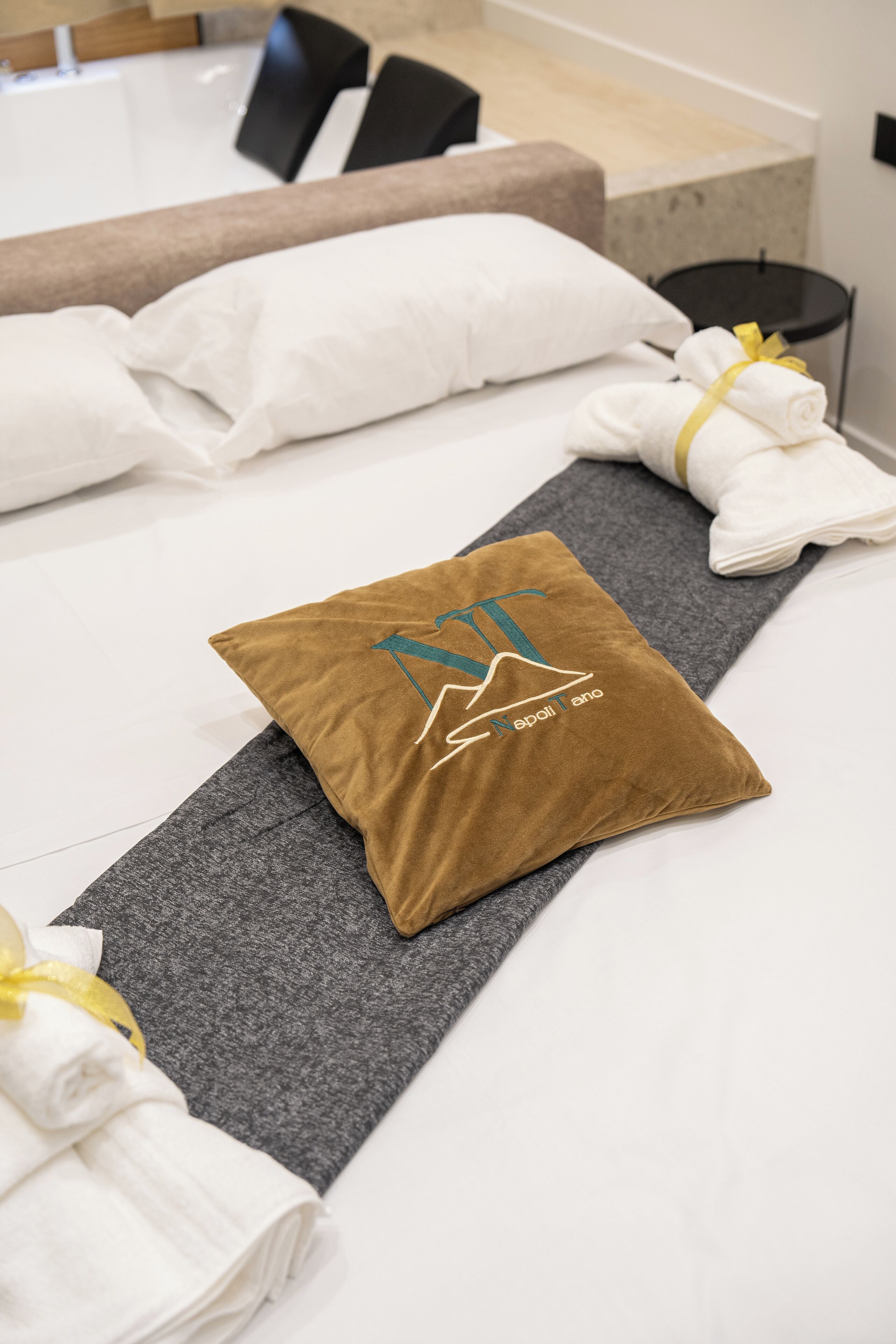 A neatly made bed with white linens, a brown pillow with a mountain design, and a yoga mat.