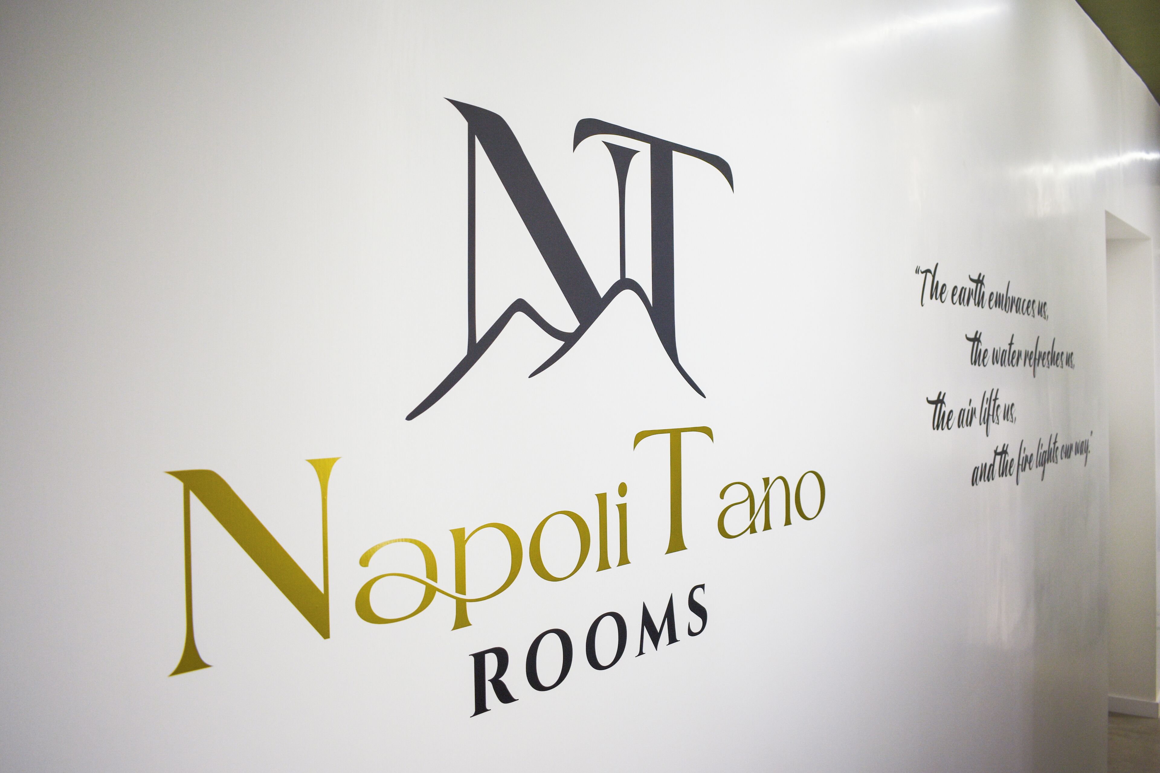 A wall with the logo and name 'Napoli Tano ROOMS' along with a decorative quote.