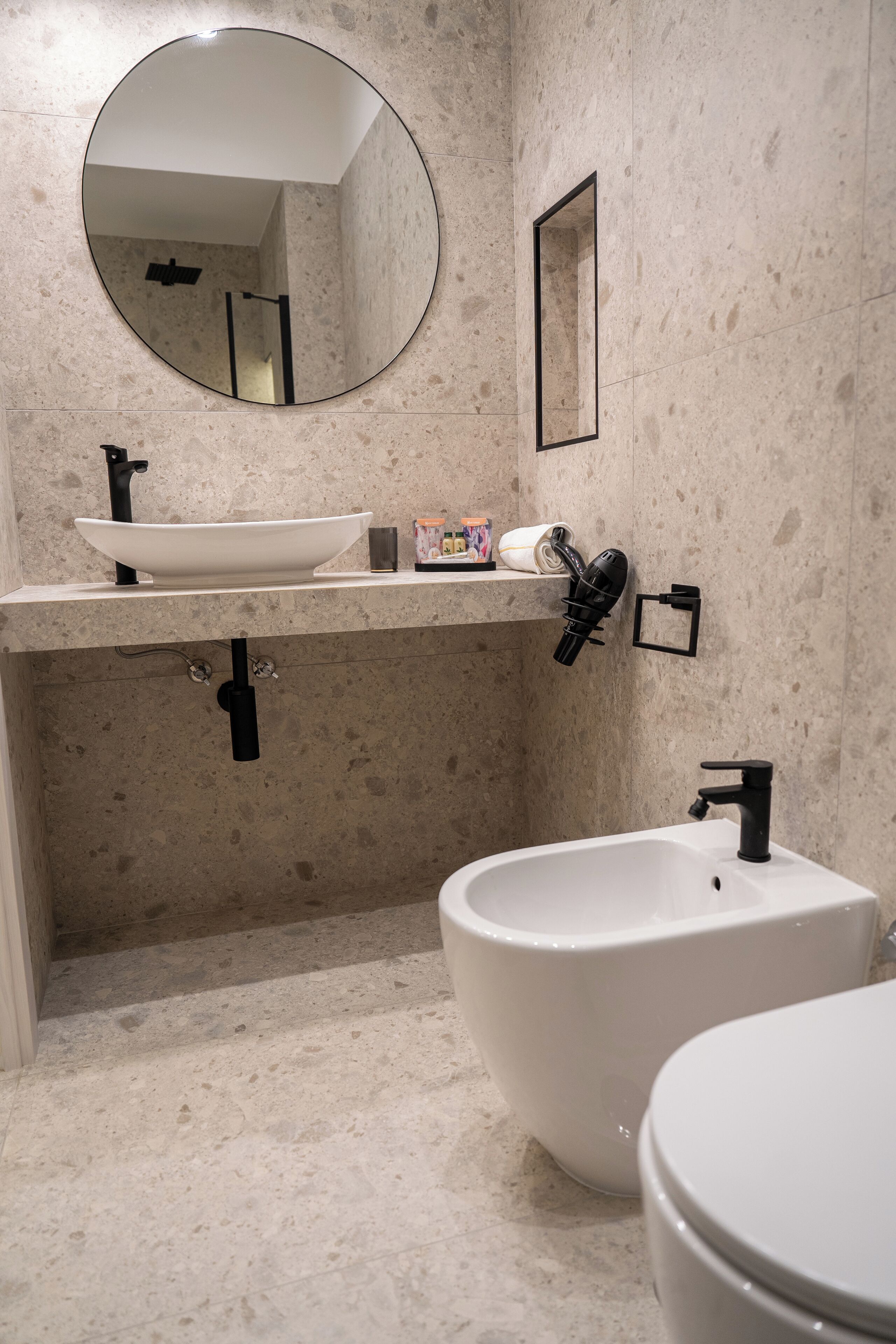 Un bagno moderno con uno specchio rotondo, un lavandino bianco, un bidet e un water.