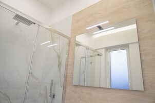 Un baño moderno con cabina de ducha de vidrio, un espejo grande y una pared decorativa de madera.