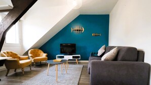 A modern living room with a TV, two armchairs, a sofa, and a blue accent wall. - Charming seaside apartment (Dinard)