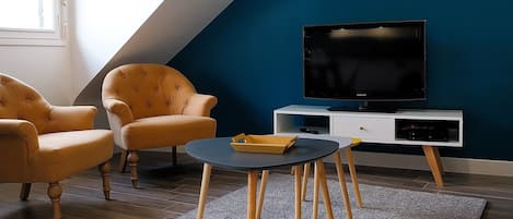 A modern living room with a sloped ceiling, a television on a white stand, two yellow armchairs, a round coffee table, and a grey rug.