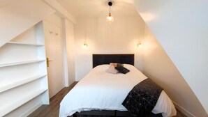 A bedroom with a bed, a sloped ceiling, and a staircase. - Charming seaside apartment (Dinard)